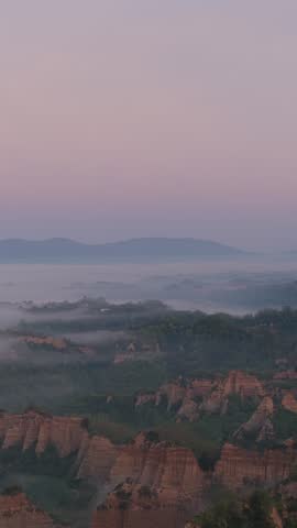 Aerial view of the unique rock formations of Valdarno shrouded in morning mist under a soft pink sky in Florence, Tuscany, Italy.