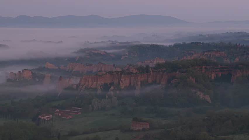 Aerial view of the Valdarno clay cliffs emerging from morning mist and fog over the rolling hills of the Tuscan landscape Florence, Tuscany, Italy.