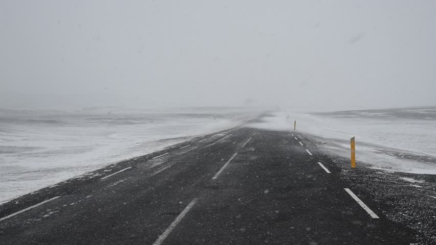 Point of view from a car driving on a lonely asphalt road during a heavy blizzard. Severe weather conditions and strong wind in iceland