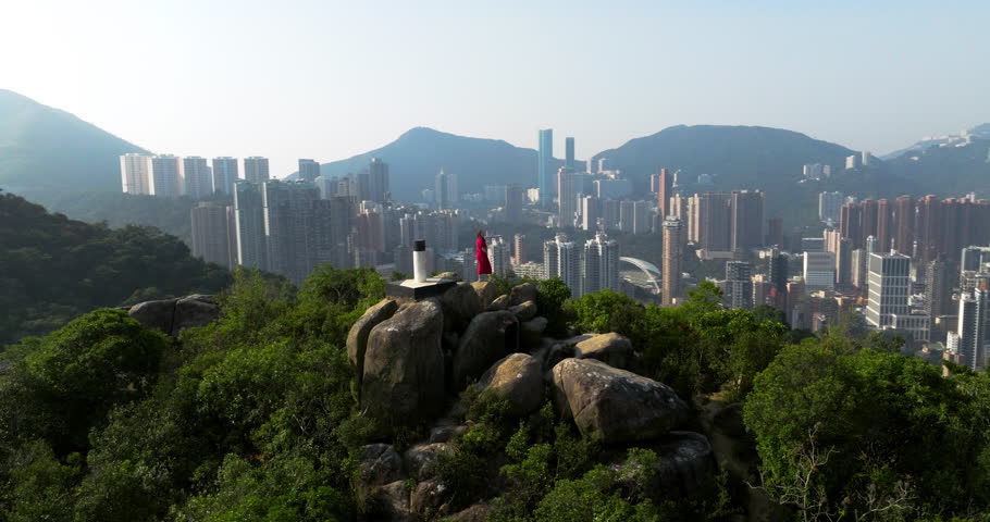 A Woman Wearing Red Dress At Braemar Hill Viewpoint Overlooking High-rise Buildings And Residential Areas Of Hong Kong Island. Aerial Rotate Shot