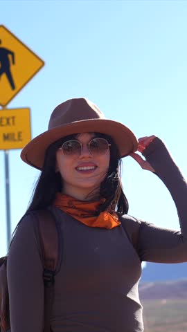 Cheerful young female hiker with a backpack and hat smiling while enjoying the beautiful desert scenery of monument valley in arizona, exploring the iconic american southwest on a sunny day