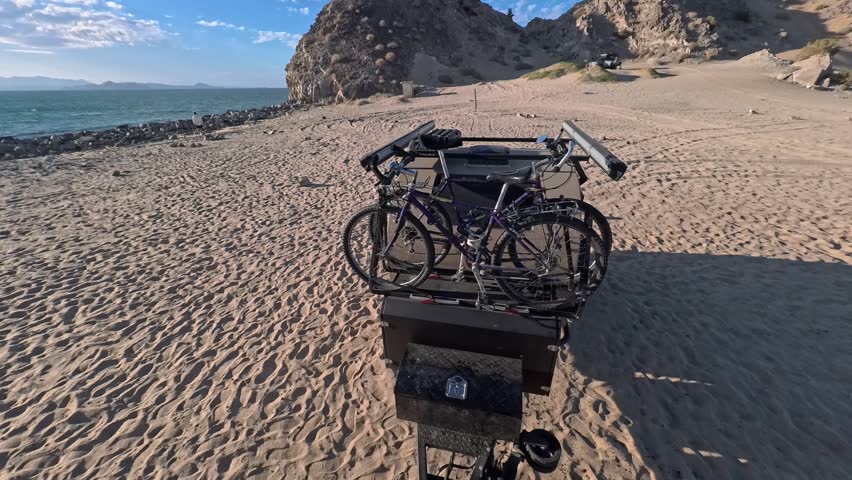 Teardrop camper trailer travels through sand on the beach at Gonzaga Bay in Baja California Mexico while carrying bikes on top