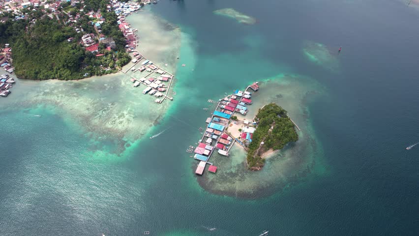 Aerial view of traditional stilt houses built over coral reefs and a small lush island in the turquoise waters of the bay in Jayapura, Papua, Indonesia.