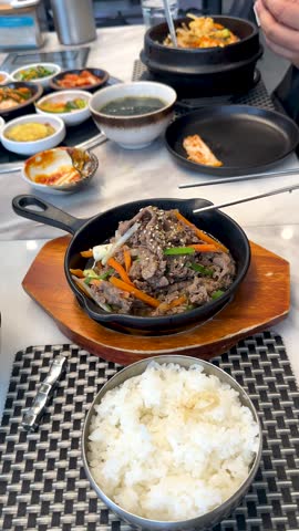 Close-up shot of a hand using chopsticks to pick up beef from a sizzling skillet