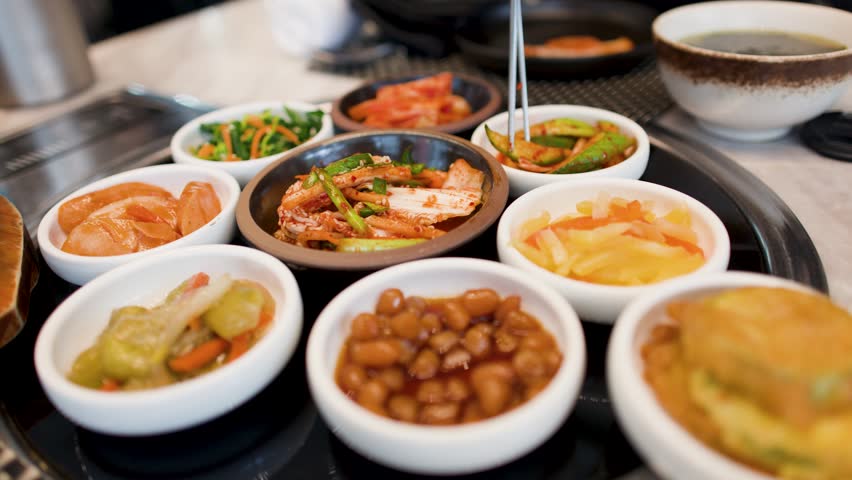 Close-up shot of various Korean side dishes including kimchi and fermented vegetables on a table