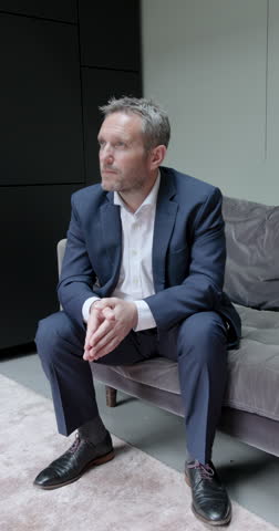 Portrait of Mature Businessman Looking at camera, sitting on Sofa in Corporate Office wearing Suit