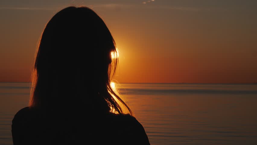Woman silhouette against beautiful sunset over serene lake.