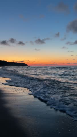 Beautiful sunset over the sea with waves and orange sky. Scenic coastal landscape during twilight.