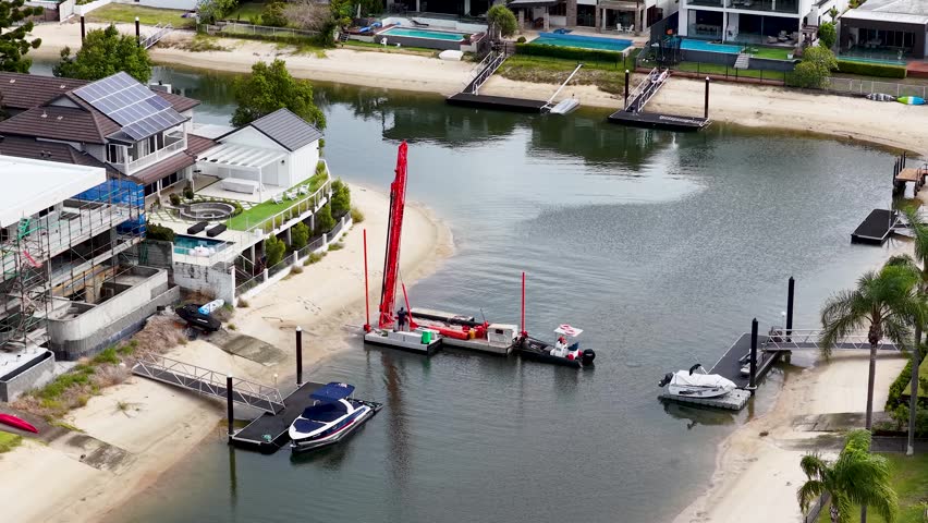 High angle aerial shot of a red crane barge performing dredging in a luxury canal