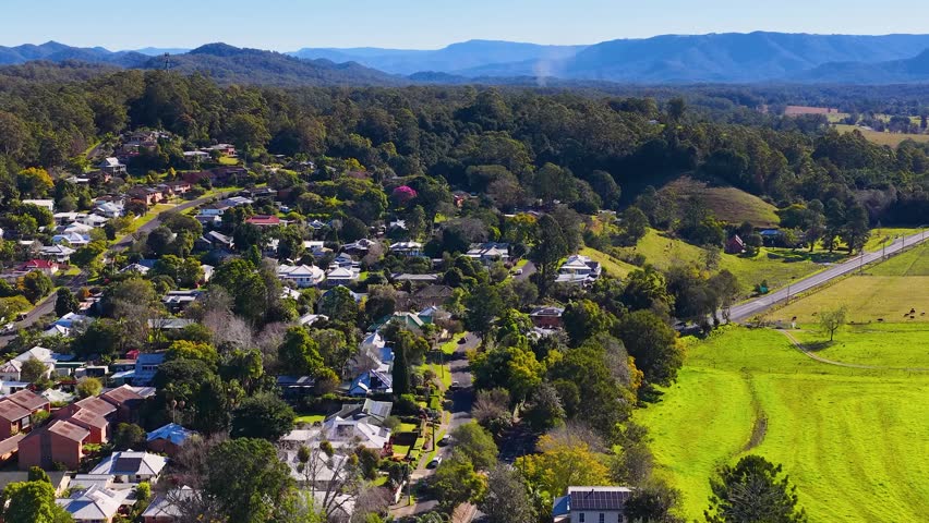 High angle drone shot reveals suburban houses nestled within lush green trees and rolling hills