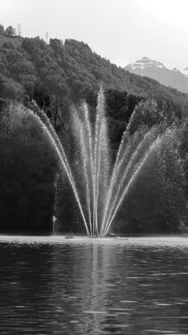Vertical monochrome shot of symmetrical water fountain creating minimal patterns on lake, ideal for abstract and background use.