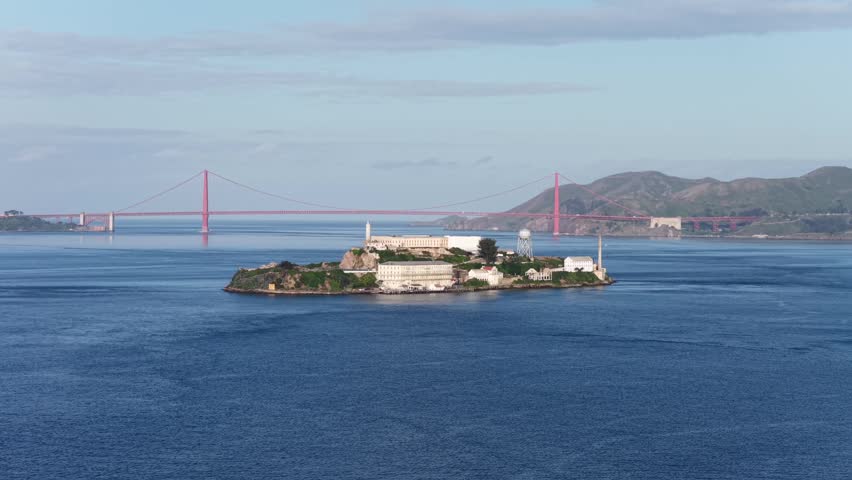 Alcatraz Island with historic prison buildings and water tower in San Francisco Bay, with Golden Gate Bridge and Marin Headlands in background. Aerial drone panorama view. Famous island in USA.
