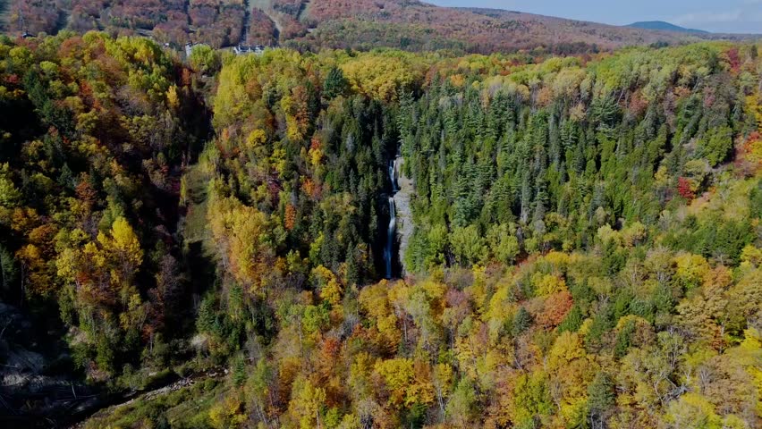 Cinematic drone flight moving forward towards the stunning Jean-Larose waterfall in Quebec. Surrounded by vibrant autumn forest and rocky cliffs.