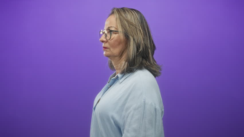 Hispanic woman wearing glasses, face visible, looking sideways against a purple studio backdrop; maturity contemplation.
