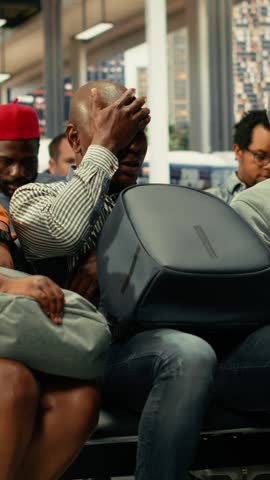Exhausted people waiting for delayed express bus transportation at busy international bus terminal during rush hour. Diverse passengers with baggage showing travel fatigue, yawning.
