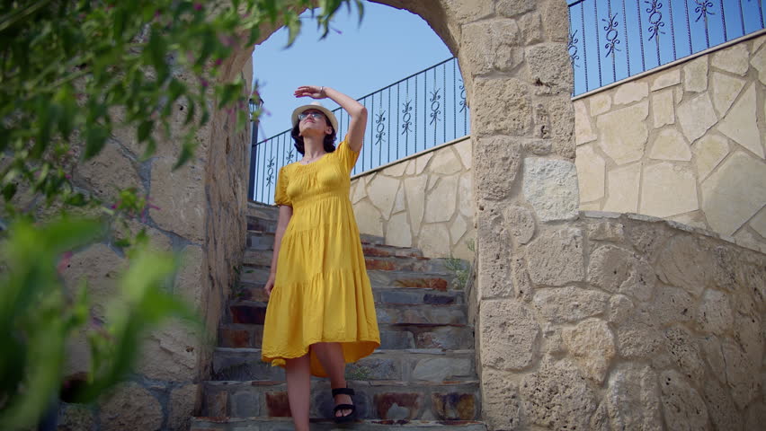 Brunette Woman in Hat Descending Stone Stairs Under Blue Sky