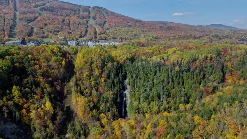 Cinematic drone flight descending and moving forward towards the powerful Jean-Larose waterfall in Quebec, Canada. Surrounded by lush autumn forest.