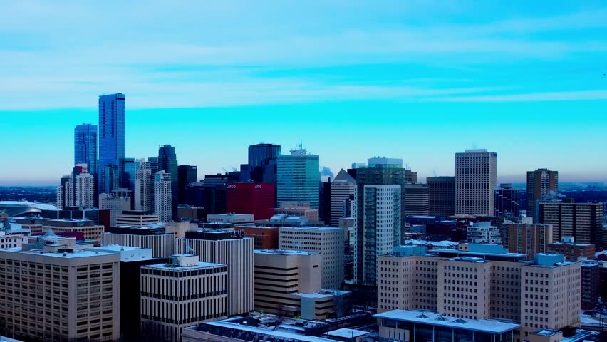 Edmonton city skyline in winter with skyscrapers, downtown buildings, and morning light. Cinematic footage captures the urban landscape with snow-dusted roofs against a clear blue sky, highlighting motion.