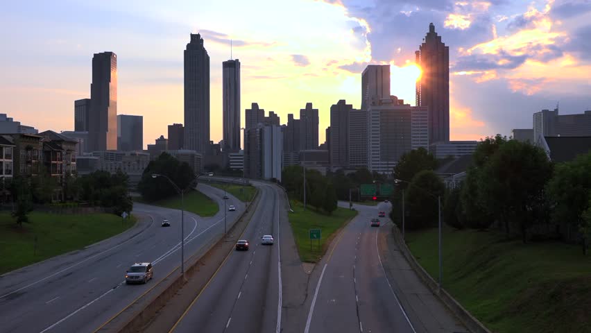 Dynamic motion of cars on a highway with the Atlanta city skyline bathed in the warm glow of a golden hour sunset, showcasing urban infrastructure and beautiful evening light.