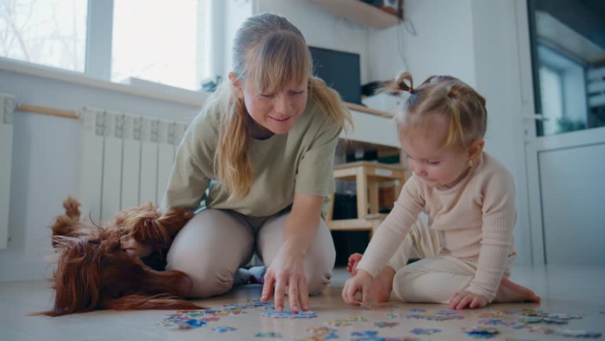 Mother and toddler focus on colorful puzzle on floor. Soft light fills room with calm, cozy feel. Dog rests nearby, adding warmth to scene. Ideal for family bonding, early childhood education