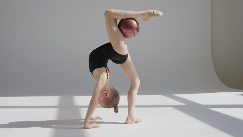 Little gymnast posing with a ball on a white background. 