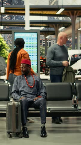 Man in african traditional clothes sitting in bus station for long-haul journey, traveling by intercity coach with big luggage for relocation. Passenger waiting for highway bus departure.