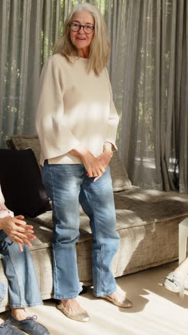 Vertical video: Pals seeing kneeling woman holding blue file senior woman rising on sofa using file. Livingroom, casual, conversation, naturallight, elderly, notebook, vertical video