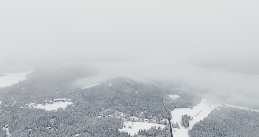 Drone flies over snow-covered Adirondack forest and mountain ridges disappearing into thick winter fog after fresh snowfall near Lake Placid, New York.