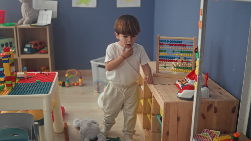 Boy presses buttons on a toy cash register and slides abacus beads at a wooden table in a building; quiet concentration.