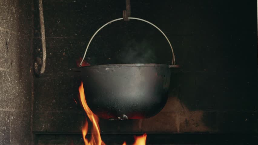 Large cauldron pot over open fire with steam rising.