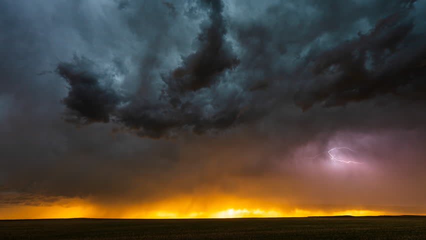 Lightning streaks across dark storm clouds as warm orange sunset tones glow along the horizon, creating dramatic contrast, intense atmosphere, vibrant sky colours and a cinematic severe weather scene