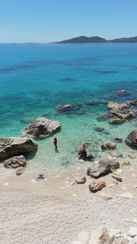 A couple experiences the tranquil beauty of Kas, Turkey, where turquoise waves kiss sun-kissed shores. Explore rocky coastlines as visitors embrace the refreshing sea on a sunny day.