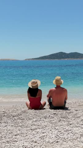 Two friends unwind on the beautiful pebbled beaches of Kas, Turkey, enjoying the serene blue waters and sunny skies. A perfect spot for holiday relaxation and coastal adventures in Antalya.