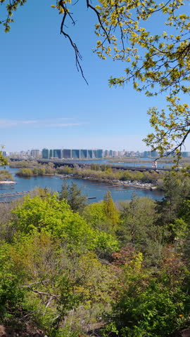 Beautiful panoramic view of Kyiv city skyline with Dnieper river and green spring forest under clear blue sky. Scenic urban nature landscape in Ukraine