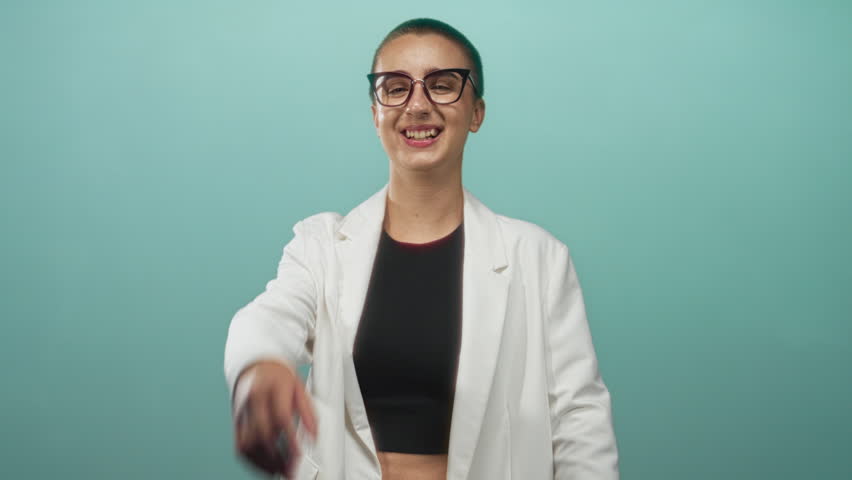Woman in white blazer pressing hand to forehead while smiling and half covering face in studio; playful amusement.