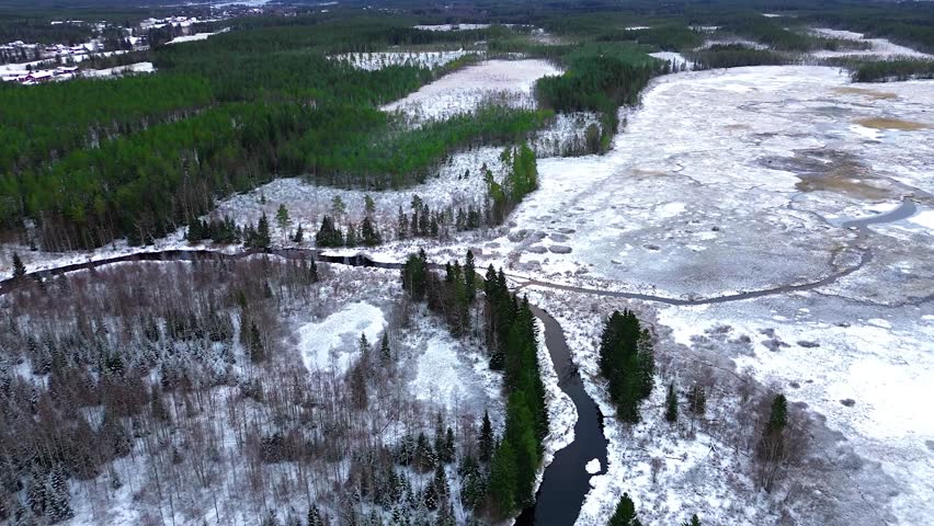 An aerial shot of a winter landscape featuring a frozen river, stream, and snow-covered forest with evergreen trees