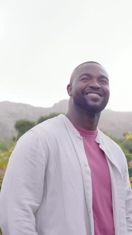 Vertical video: Smiling man laughing while looking upward at hills, camera zooming in, mauve shirt. Outdoors, nature, hillside, mountains, candid, joy, vertical video