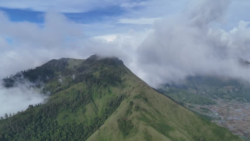 Aerial View of Majestic Green Mountains Covered by Rolling White Clouds on a Clear Day