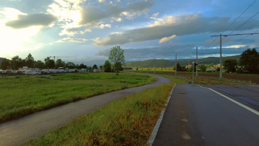 Paved walking path next to an asphalt road with fields and a railway line on the right