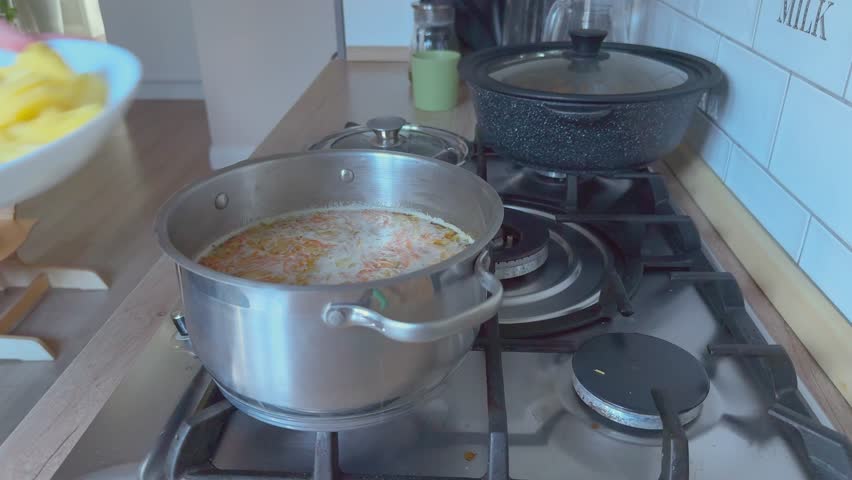 Chopped potatoes added into soup pot cooking homemade meal in kitchen. 
