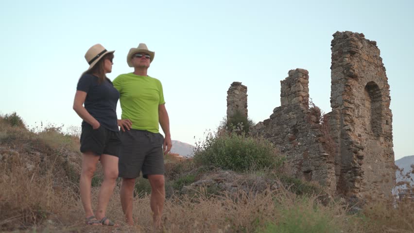 Couple of tourists in hats exploring ancient stone ruins on sunny summer vacation day