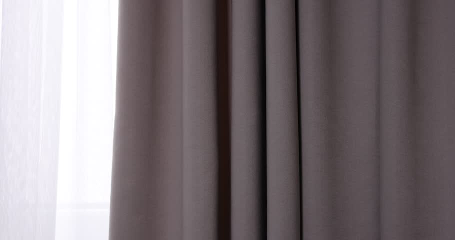 Woman fastening dark beige curtain with tieback indoors, closeup