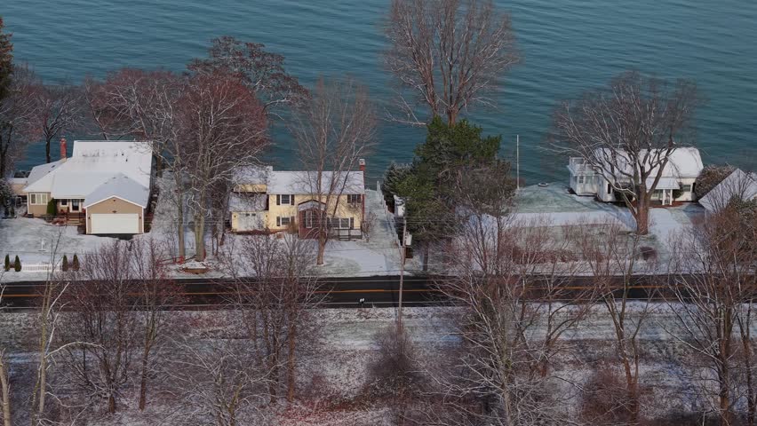 Bird eye view of winter houses, lake shore, snow covered trees.