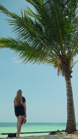 Woman enjoys tropical ocean view, peaceful beach, tall palm tree.