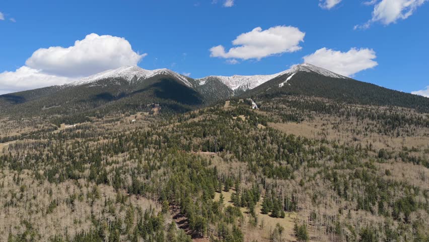 4K drone video captures the slopes of Arizona Snowbowl. Cinematic flying footage shows skiers on snowy runs surrounded by pine forests and rugged mountain peaks under a blue winter sky.