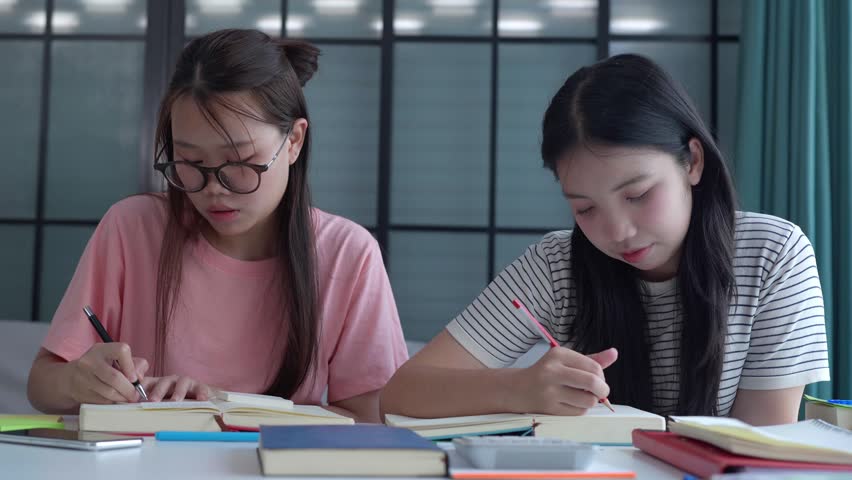 Two Asian girls doing homework together in living room.