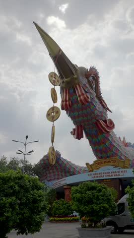 Colorful giant dragon sculpture rises above a Vietnamese theme park entrance under dramatic cloudy skies during daytime.