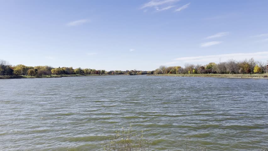 A vast landscape of a lake on a windy autumn day with light clouds and seasonal foliage.