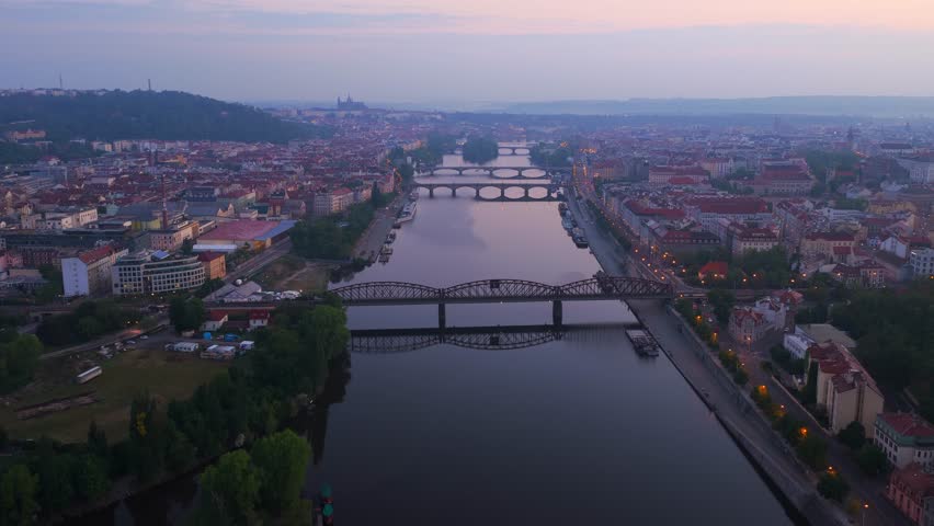 Aerial view of the Vltava river and historic bridges under a soft dusk sky with Prague Castle on the horizon in Prague, Prague, Czechia.