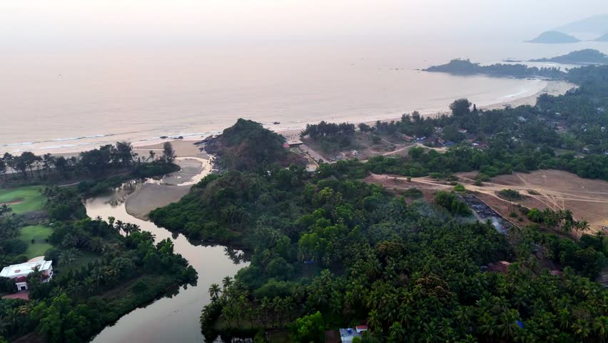 Cinematic aerial view of Canacona showcasing a winding river flowing through dense tropical greenery toward a serene sandy coastline beside the Arabian Sea.
